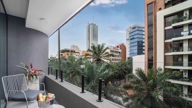 Un balcón con vistas a un paisaje urbano, que incluye edificios altos y palmeras.