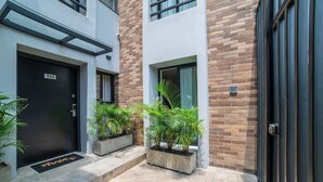 A modern building with a black door labeled "101", a small window with a curtain, and potted plants on the ground. - Luxury 3-Bed | Walk to Boulevar & Granada | E101 (Cali)