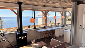 Una cabaña acogedora con estufa de leña, comedor y cocina con amplias ventanas que dan a un paisaje pintoresco.