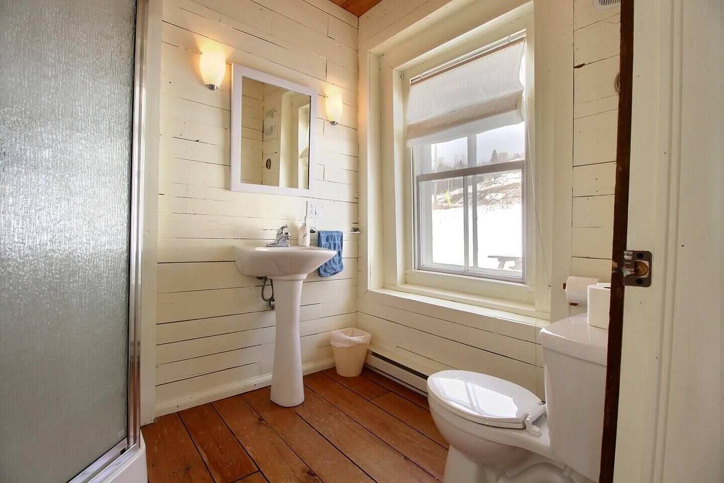 A small bathroom with a white sink, a mirror, a toilet, and a window with a view of the outside.