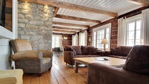 A cozy log cabin interior with a stone wall, wooden beams, and a mix of wicker and leather furniture.