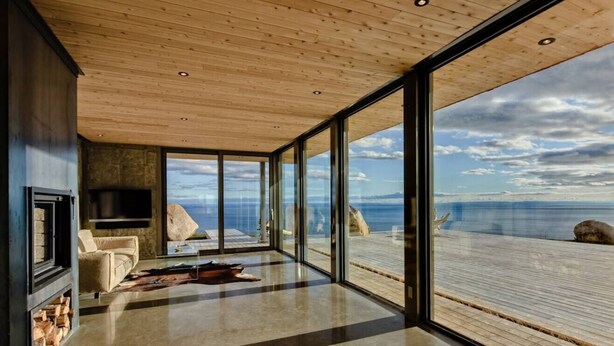 A modern interior with large windows, a fireplace, and a view of the sea. - Chalet Marée Basse | Charlevoix (La Malbaie)