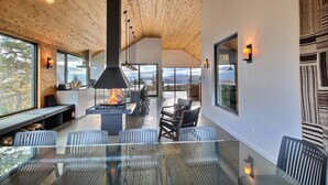 A modern kitchen with a central wood-burning stove, large windows, and a dining area with glass tables and chairs.