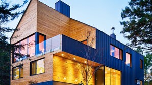 A modern two-story house with large windows, a wooden facade, and a blue exterior.