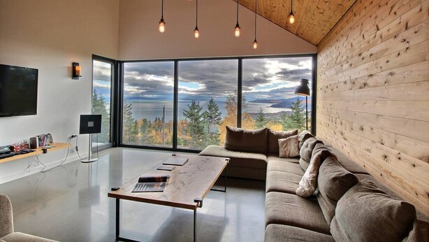 A modern living room with a large window offering a scenic view, a flat-screen TV, and a wooden ceiling.