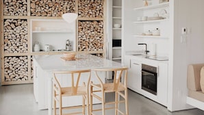 A modern kitchen with a central island, wooden cabinets, and a built-in wood storage wall.
