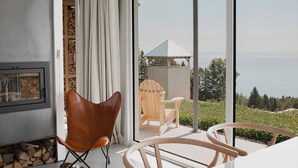 A modern living space with a fireplace, a dining area with chairs, and a view of a wooden structure and greenery.