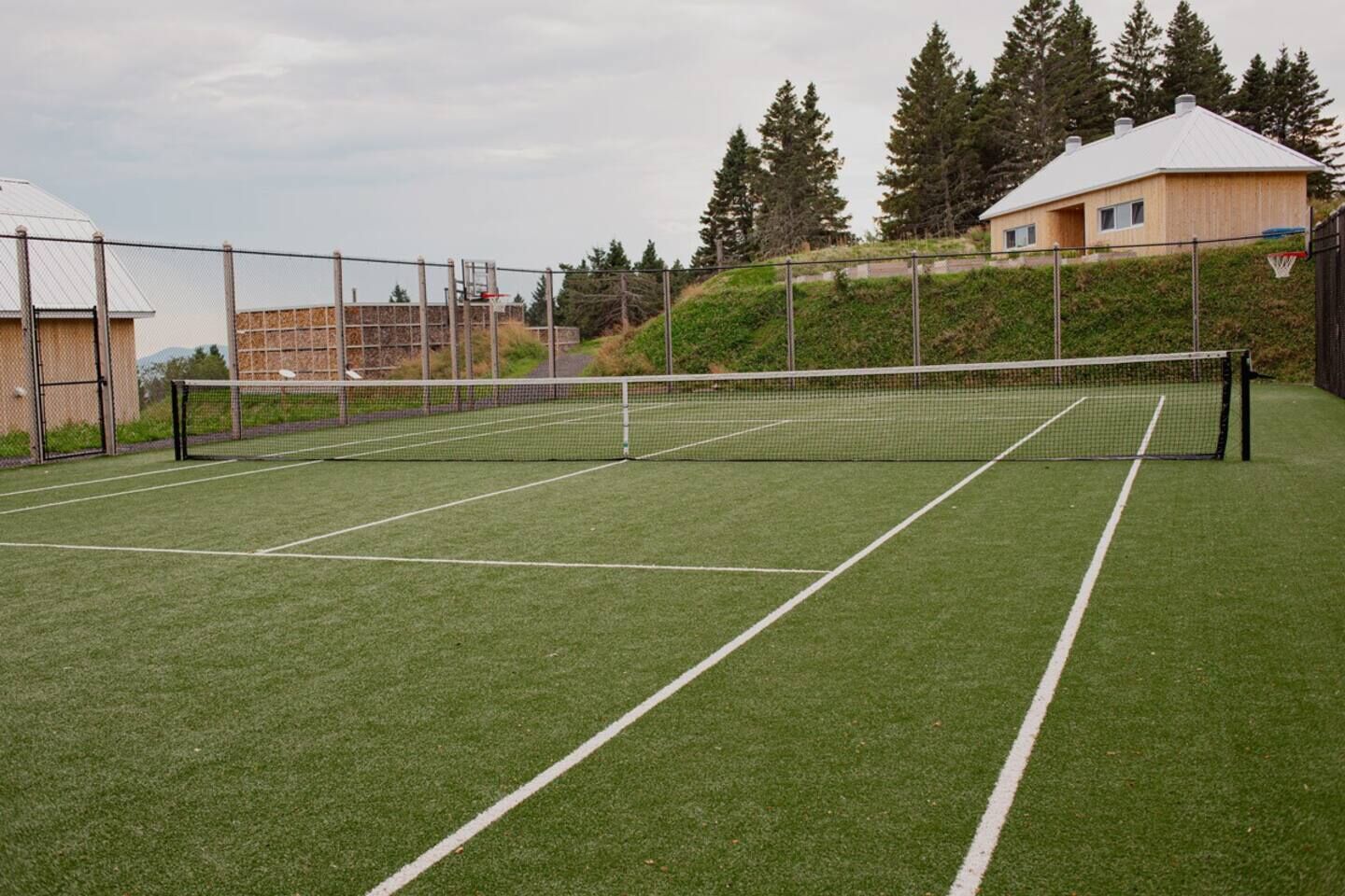 Un campo da tennis con una rete, circondato da una recinzione e alberi.