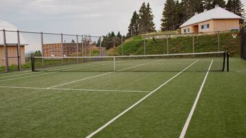 Un campo da tennis con una rete, circondato da una recinzione e alberi.