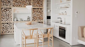 A modern kitchen with a central island, wooden cabinets, and a built-in wood storage wall. - Chalet Le Petit Rondin #3 | Charlevoix (La Malbaie)