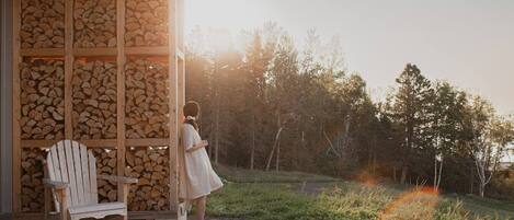 A wooden chair and a person standing near a stack of firewood outside a building.