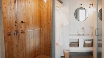 Een houten douchecabine met een glazen deur, een witte badkamer met een ronde spiegel en een wastafel met een witte wasbak.