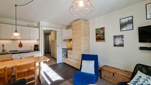 A modern kitchen with wooden cabinets, a dining area with a wooden table and chairs, a blue armchair with a white pillow, and a television on the wall. - 300m from ski lifts, 1st floor, tv, ski locker, 40m², Flaine (Flaine)