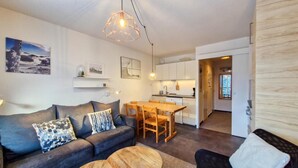 A modern living room with a sofa, coffee table, and dining area. There is a kitchen in the background with white cabinets and a wooden countertop. - 300m from ski lifts, 1st floor, tv, ski locker, 40m², Flaine (Flaine)