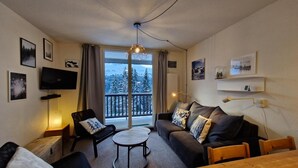 A cozy living room with a sofa, armchair, and a small round table. A TV is mounted on the wall, and there is a balcony with a view of snow-covered trees. - 300m from ski lifts, 1st floor, tv, ski locker, 40m², Flaine (Flaine)