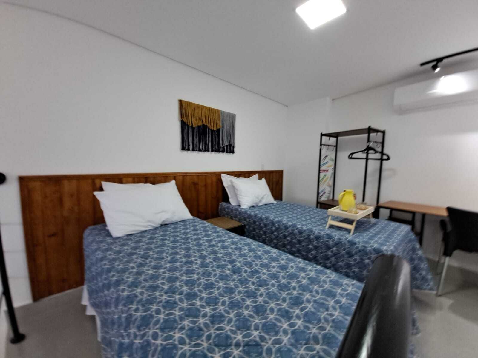 Ein Hotelzimmer mit zwei Betten, einem Schreibtisch, einem Stuhl und einer Kleiderstange.