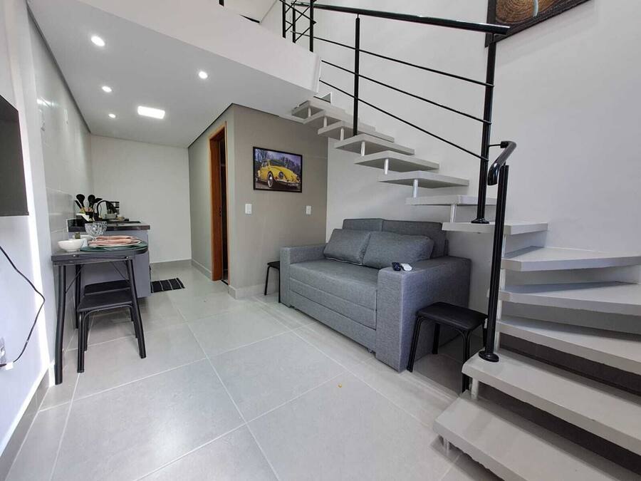 A modern living space with a grey sofa, a dining area with a table and chairs, and a staircase with a metal railing.