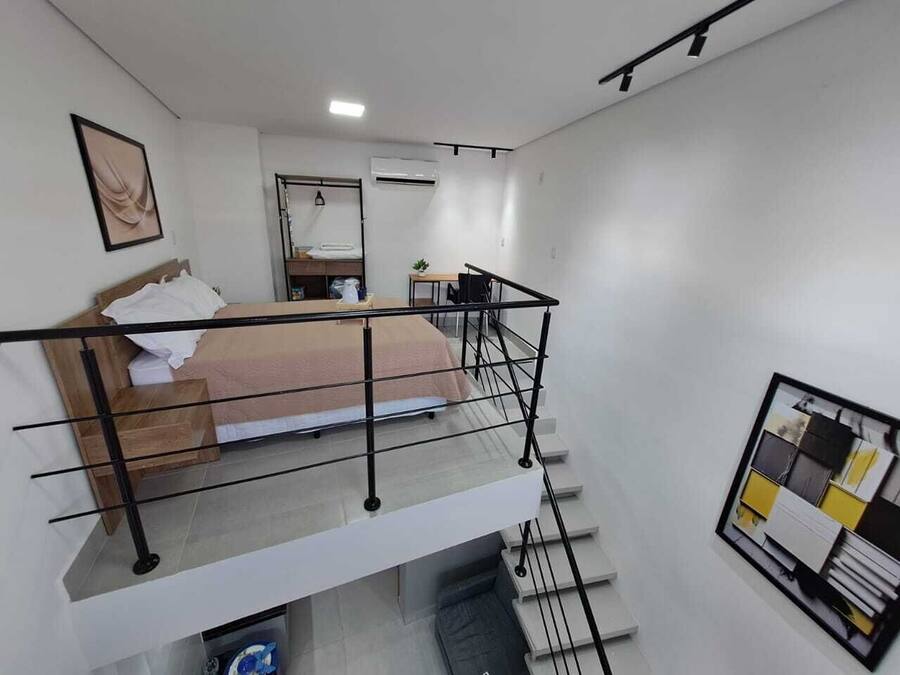 A modern hotel room with a bed, a small desk, and a balcony with a railing.