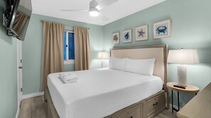 A hotel room with a bed, two bedside tables, a ceiling fan, a TV, and artwork on the wall. - Sand Cliffs 108: Steps to Beach & Pool Access! (Panama City Beach)