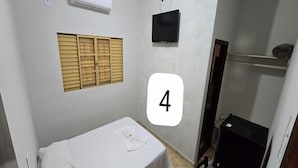 A small, single-room accommodation with a bed, a television, and a window with shutters. - Delta Hotel (Andradina)
