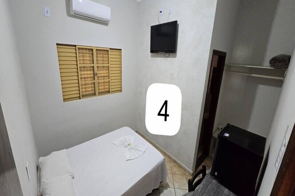 A small, single-room accommodation with a bed, a television, and a window with shutters.