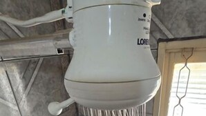 A white water dispenser with multiple hoses, mounted on a tiled wall with a window in the background. - Delta Hotel (Andradina)