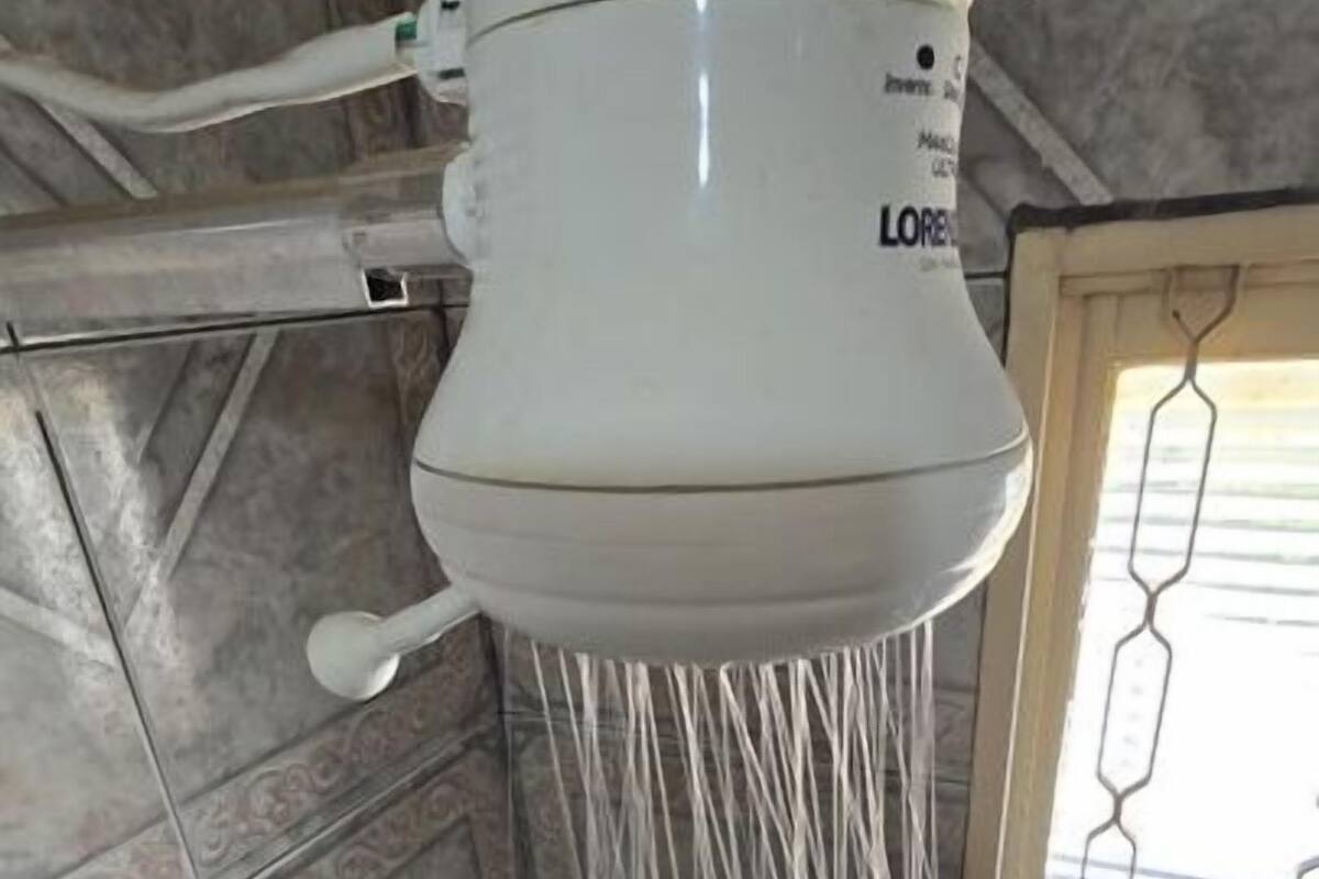 A white water dispenser with multiple hoses, mounted on a tiled wall with a window in the background.