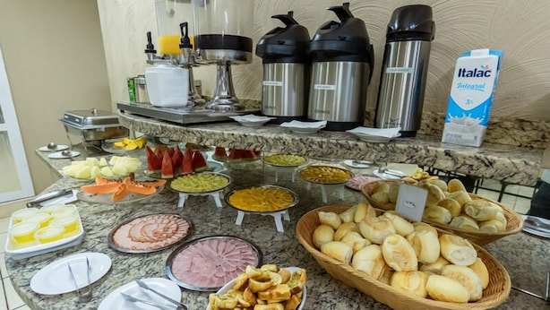 A buffet with various food items and condiments, including bread, pastries, and a carton of milk. - Delta Hotel (Andradina)