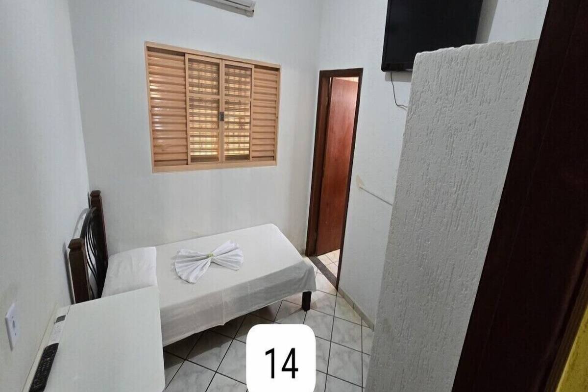 A small, clean room with a bed, a window with wooden shutters, a television mounted on the wall, and a door.