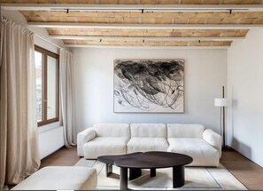 Una sala de estar moderna con un sofá blanco, una mesa de centro oscura y un cuadro abstracto grande en la pared.