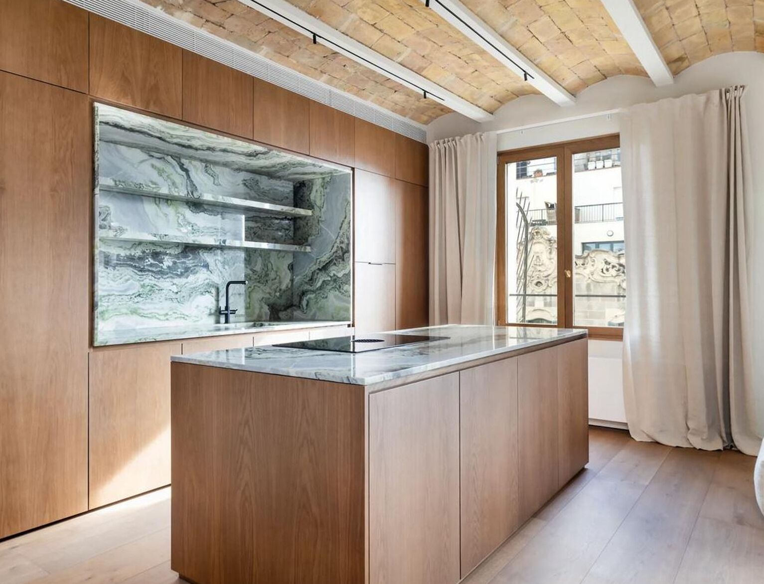 A modern kitchen with wooden cabinetry, a marble backsplash, and a large window with curtains.