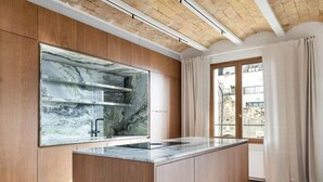 A modern kitchen with wooden cabinetry, a marble backsplash, and a large window with curtains. - Barcelona Blissful Apartment Escape (Barcelona)