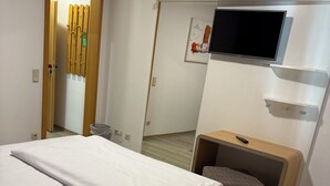A bedroom with a bed, a TV mounted on the wall, and a small bench. - Eurocity Hotel (Bruchkoebel)