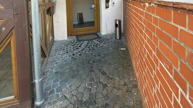 A hotel entrance with a stone-paved path, a wooden door, and a sign above the door. - Eurocity Hotel (Bruchkoebel)