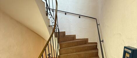 A staircase with a metal railing, beige steps, and a wall-mounted light switch.