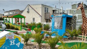 Un parque infantil con una estatua de jirafa, una cascada pequeña y un letrero que dice '¡POR FAVOR NO TOQUE Obstáculos Móviles!'.