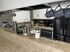 A kitchen with granite countertops, stainless steel appliances, and hanging pots.