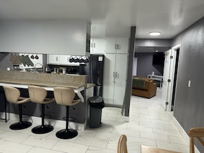A modern kitchen with a bar area, white cabinets, and a stainless steel refrigerator.