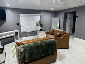 A modern living room with a sofa, a small table, a potted plant, and a fireplace.