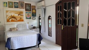 Une chambre à coucher comprenant un lit, une table de chevet, un climatiseur fixé au mur et une porte avec des panneaux de verre.