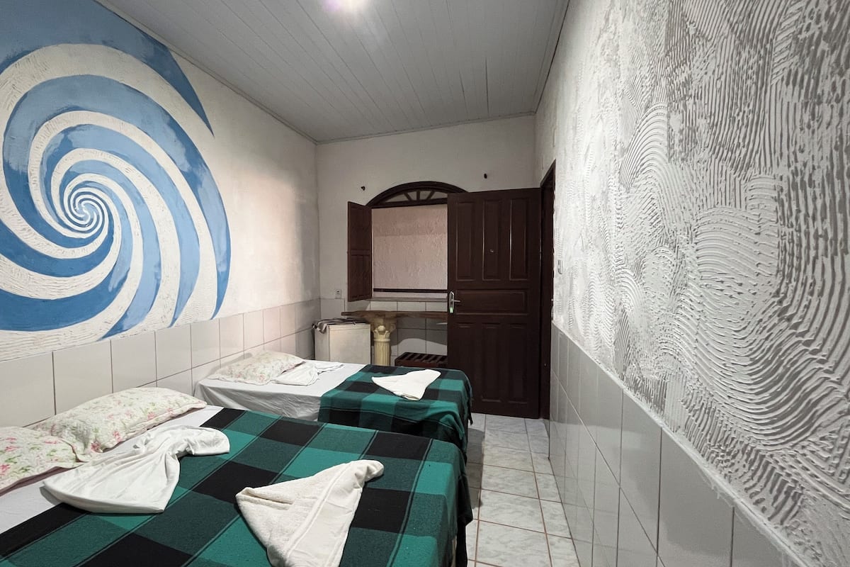 Una habitación con dos camas, una obra de arte espiral azul y blanca en la pared, un armario de madera y un papel tapiz decorado.