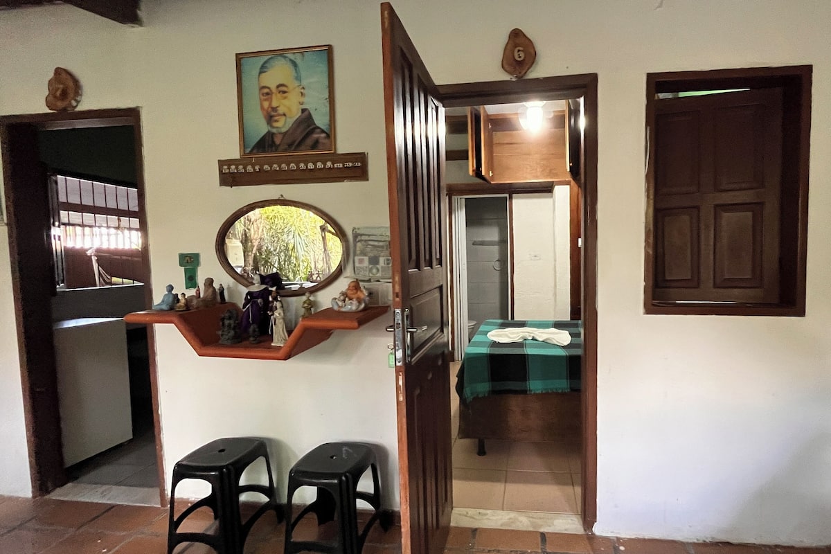 Una habitación con una cama, un espejo, una estantería con figuritas y una puerta que da a otra habitación.