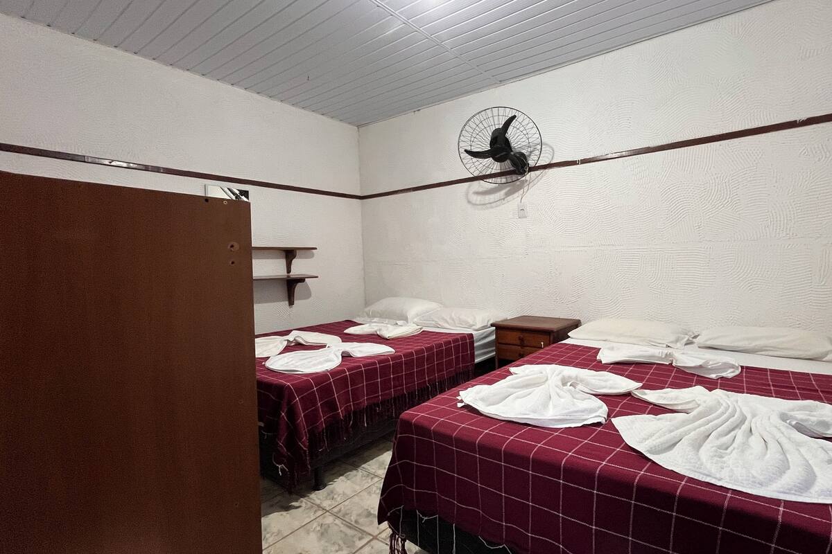Una habitación pequeña y limpia con dos camas, un ventilador y un armario de madera.