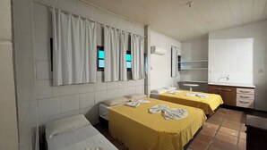 Une chambre d’hôtel avec deux lits, un petit bureau, une chaise, une fenêtre avec des rideaux et une salle de bain équipée d’un lavabo et d’un miroir.