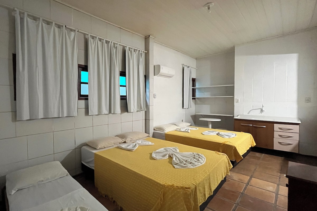 Habitación de hotel con dos camas, un escritorio pequeño, una silla, una ventana con cortinas y un baño con lavamanos y espejo.