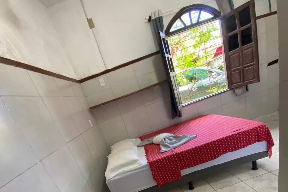 Una habitación pequeña con baldosas, una cama, un ventanal con cortinas y un radiador.