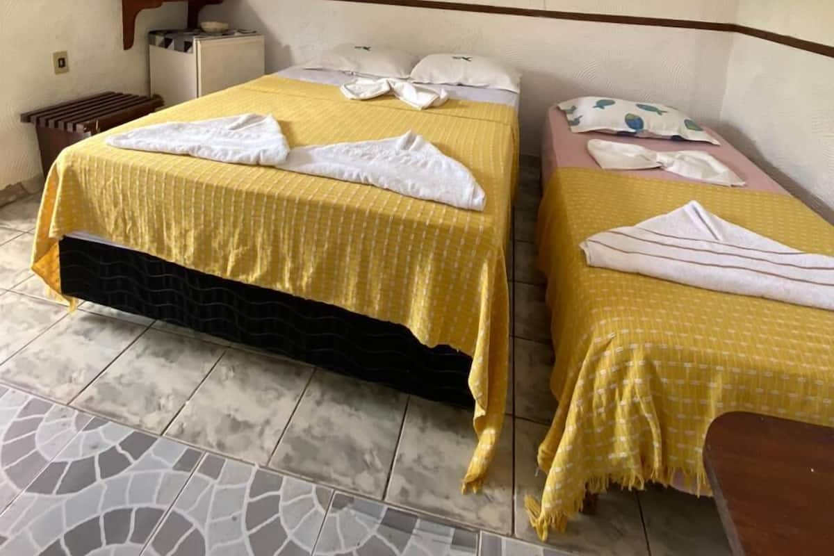 Habitación de hotel con dos camas, ventilador de techo, una mesita pequeña y suelo de baldosas.