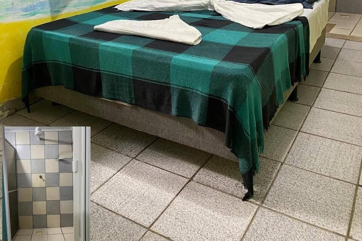 Una habitación con cama, ventana con contraventanas de madera, puerta y pared con escena de playa pintada.