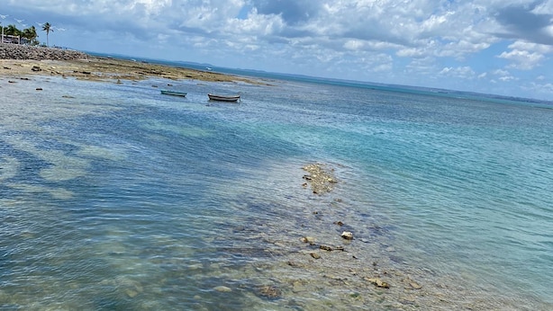 On aperçoit clairement une plage aux eaux calmes, quelques bateaux et une côte rocheuse.