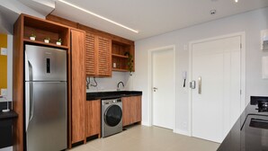 Una cucina moderna con frigorifero in acciaio inossidabile, mobili in legno, lavatrice integrata e piano di lavoro nero.